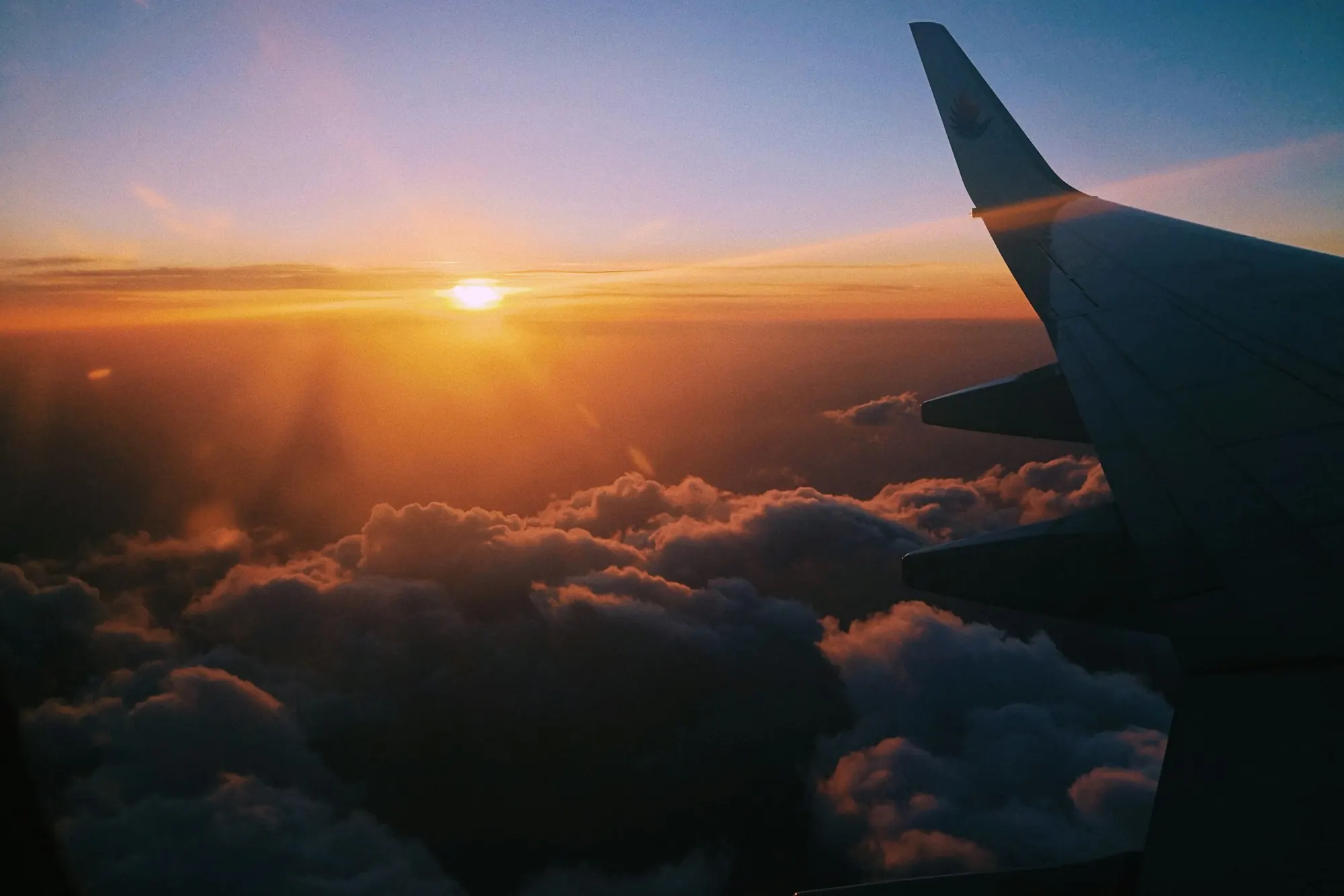 A business jet wing above a sea of cloud at sunset